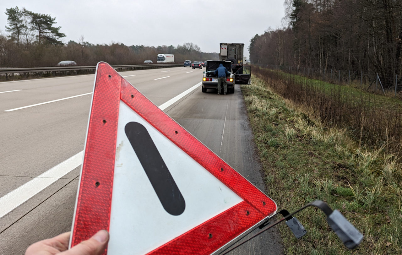 Rotes Warndreieck vor einem Mercedes, der auf der Autobahn A7 rechts auf den Standstreifen gefahren ist. 