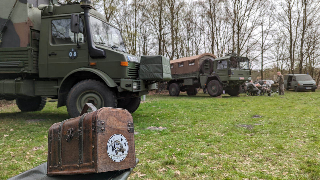 Eine kleine Holzkiste mit olivgünen Militärfahrzeugen im Hintergrund 