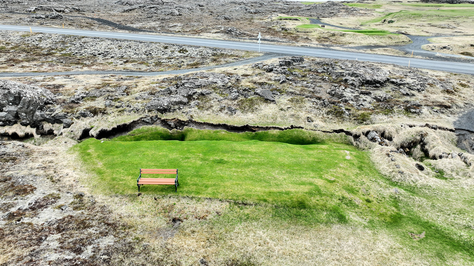 Grüner Rasen mit Parkbank und Riss in der Erde wegen Erdbeben in Grindavik Island