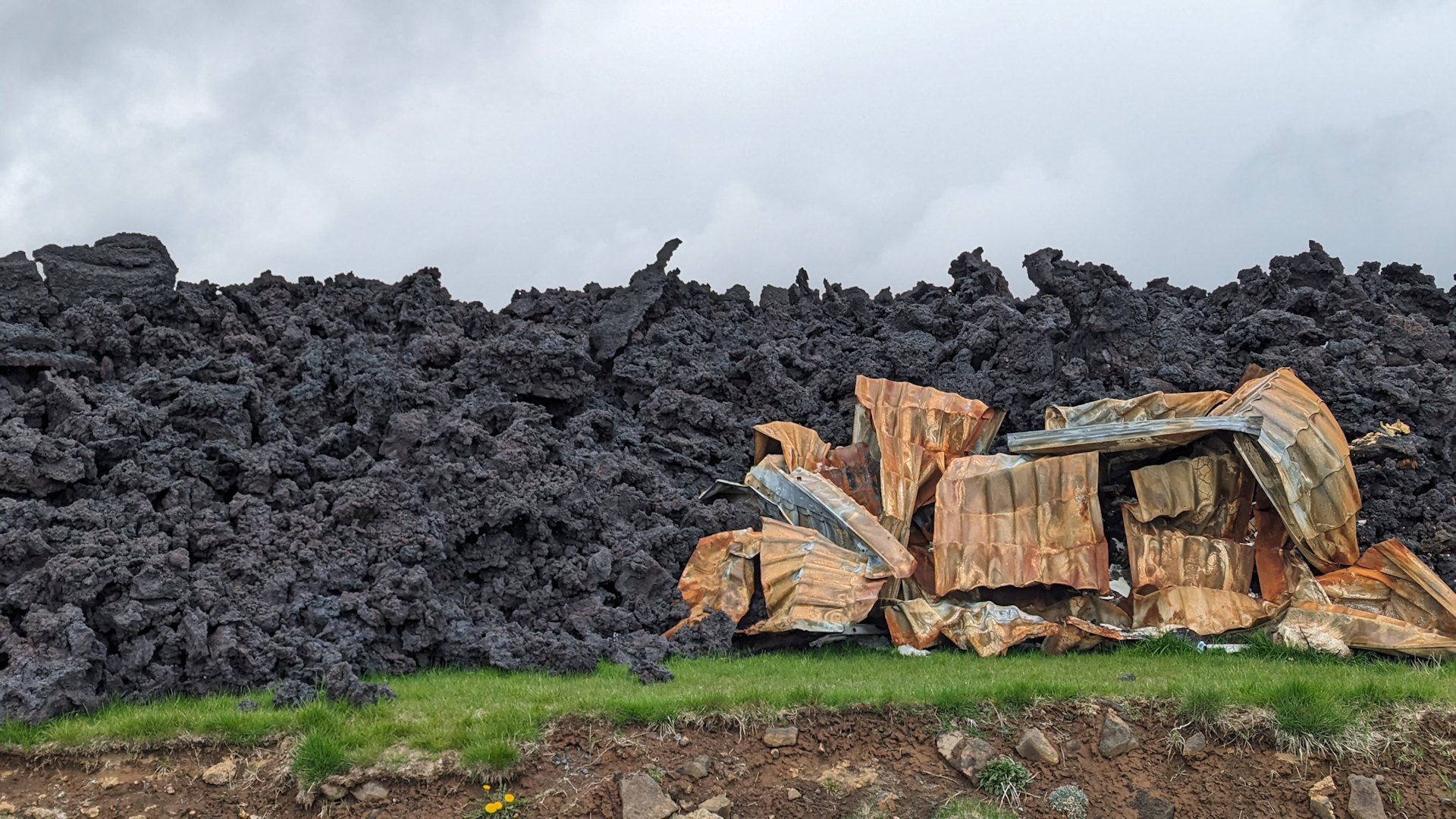Schwarze Lava hat ein Grundstück überrollt. Metallreste einer ausgeglühten Garage