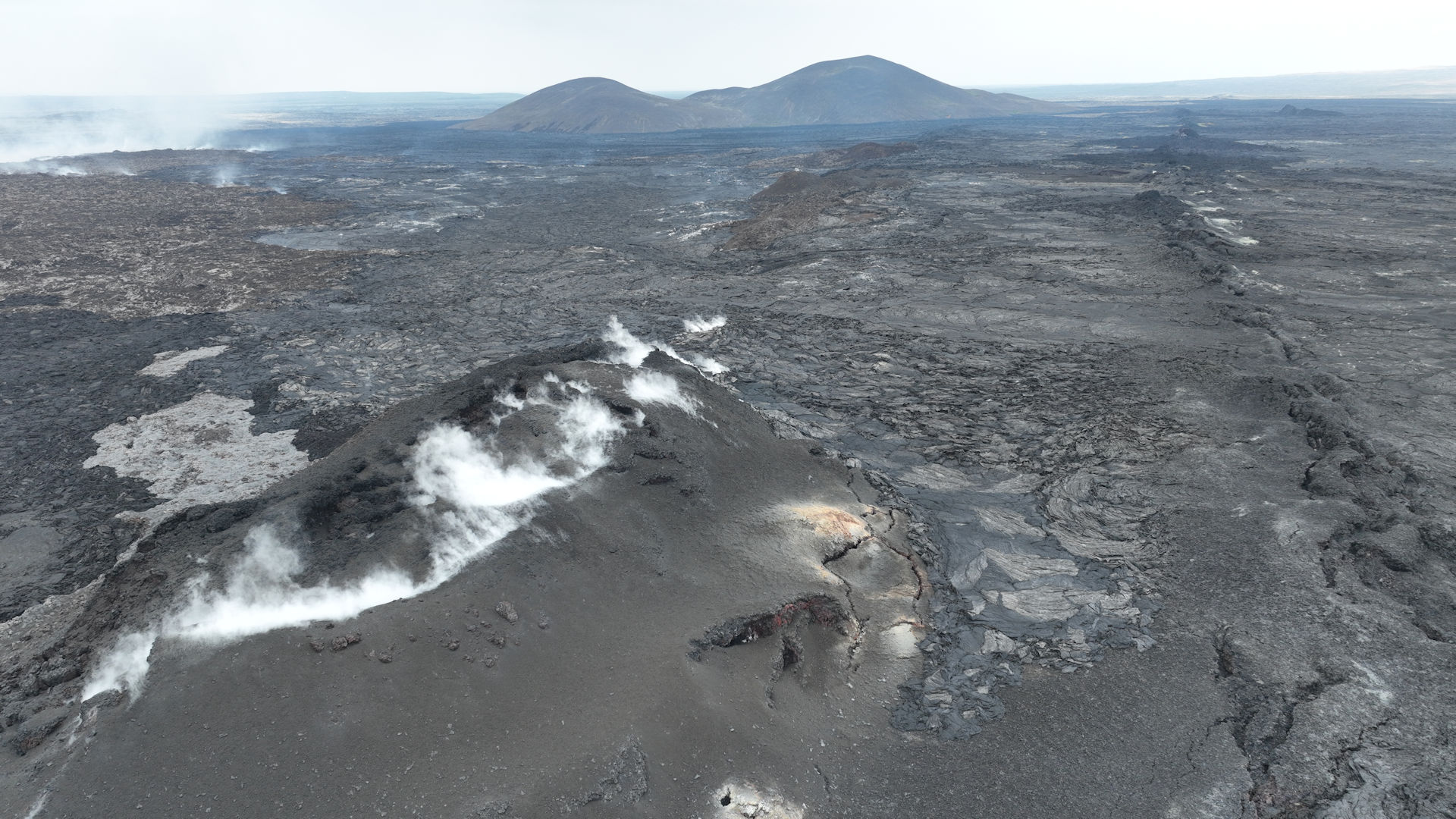 Graue Vulkanlandschaft Grindavik. Weisser Wasserdampf strömt als Wolke aus einem Vulkan Kegel in Island