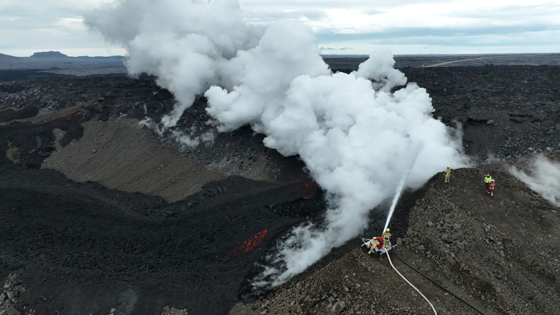 Feuerwehrleute pumpen Wasser auf Lava, was sofort in weissen Wolken  verdampft