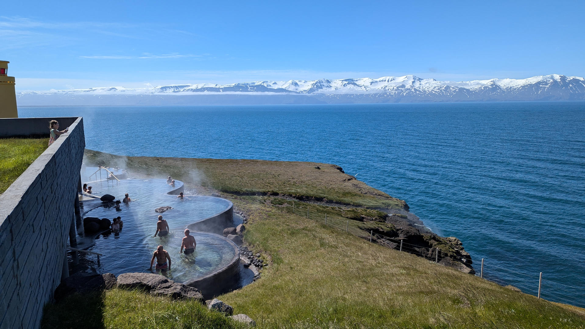 Badebecken vom Geosea Husavik mit blauem Meer und schneebedeckten Bergen im Hintergrund