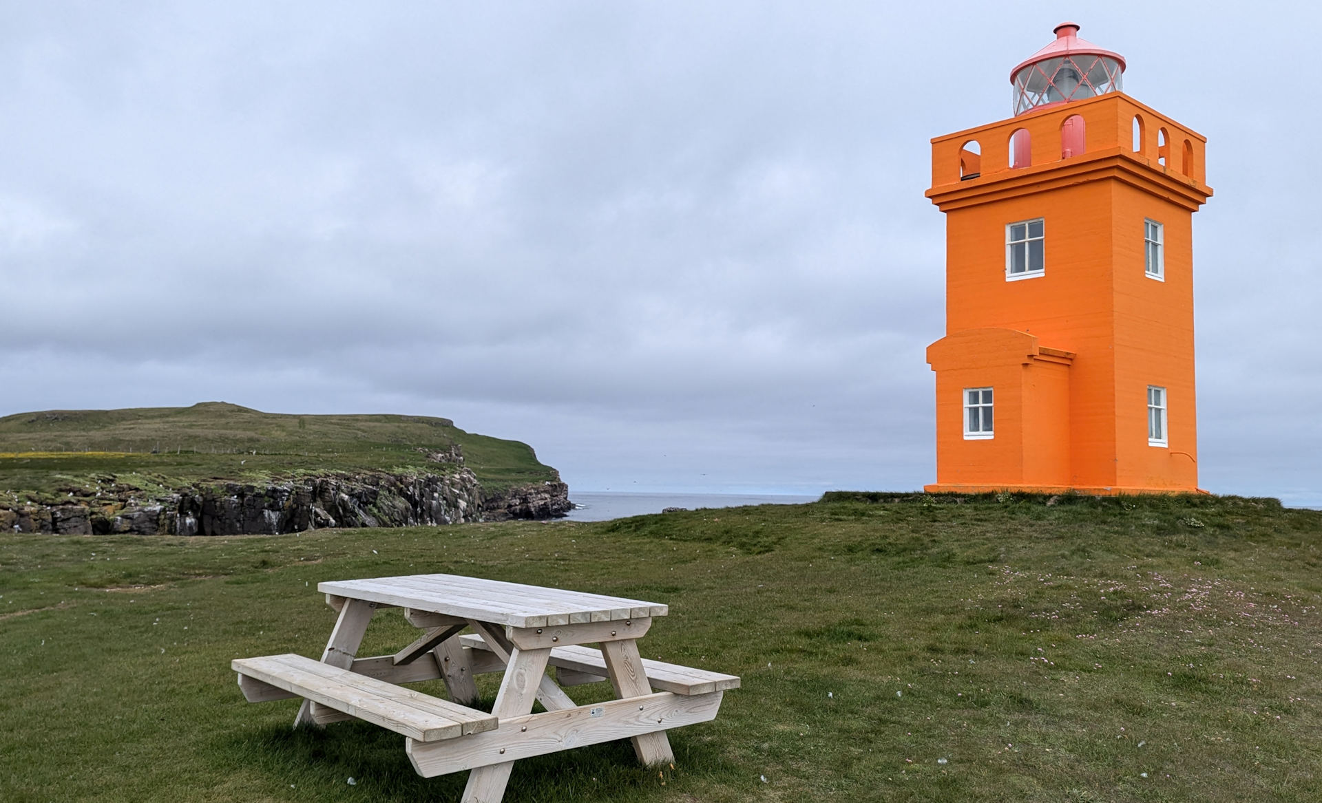 Orangener Leuchtturm mit Holzbank, in Grimsey, Island