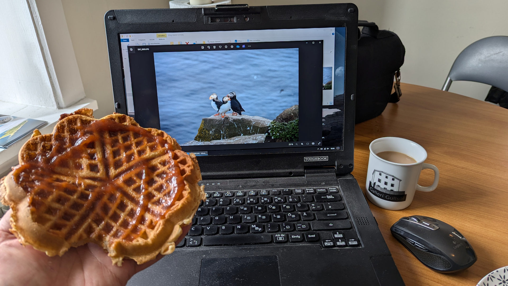 geöffnetes Notebook mit Puffin Bild in einem Cafe, eine Hand hält eine Waffel mit Marmelade