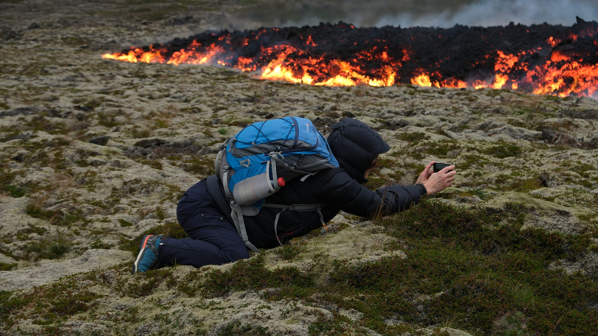 Eine Frau fotografiert auf dem Bauch liegend vorrückenede Lava in Island