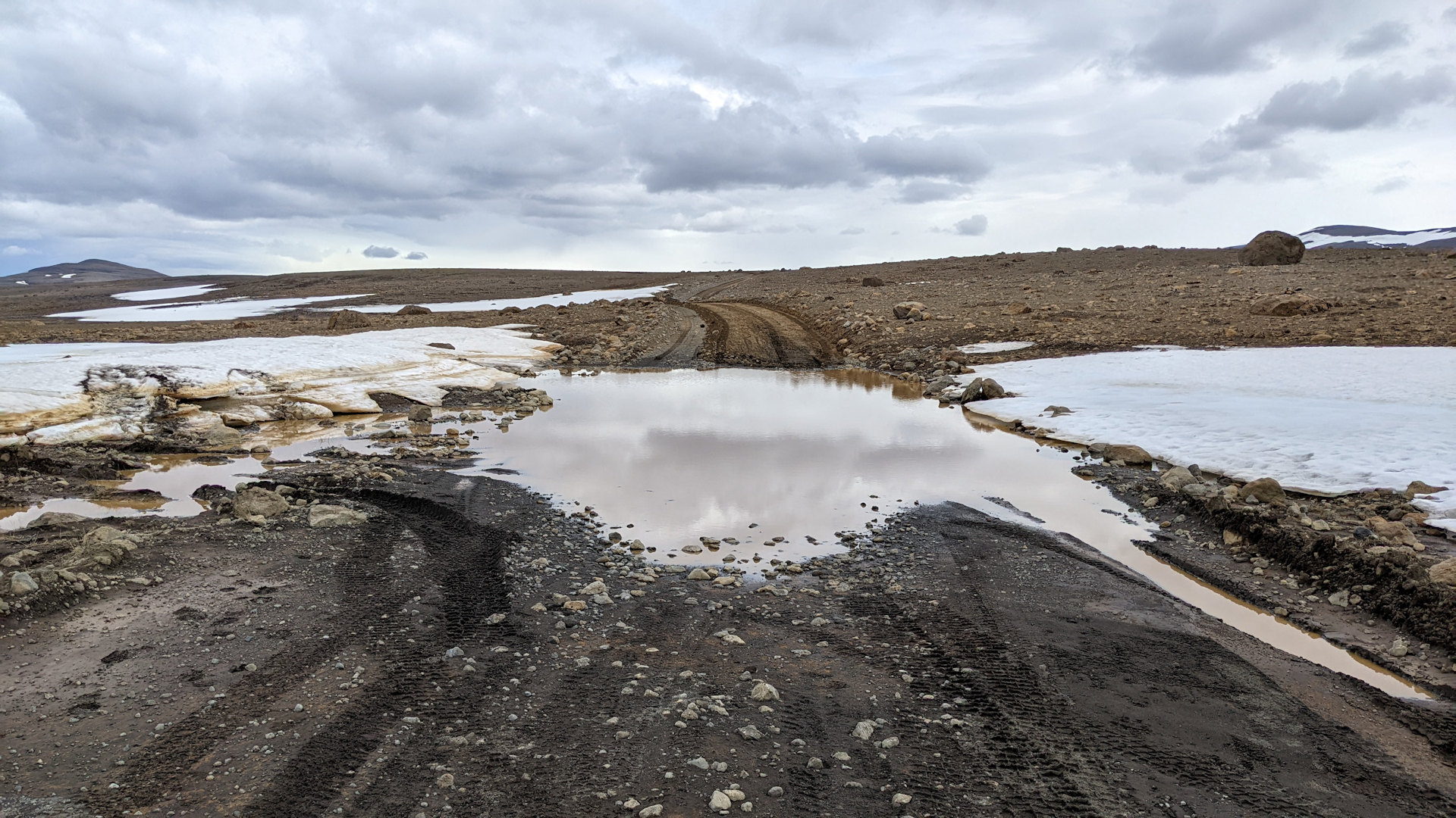 Ein kleines Stück Piste ist mit Wasser überflutet, links und rechts ist etwas Schnee. Der schmelzende Schnee hat die Fahrbahn überflutet. 