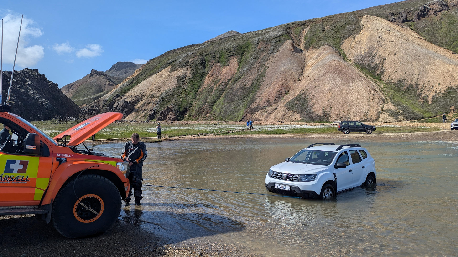 Ein Rettungswagen zieht einen weissen Dacia Duster aus einer Furt in Landmannalaugar, Island