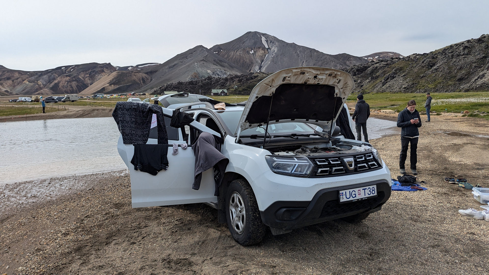 Liegen gebliebener weisser Dacia Duster mit geöffneter Motorhaube und Türen, an denen Anziehsachen zum trocknen aufgehängt sind. 