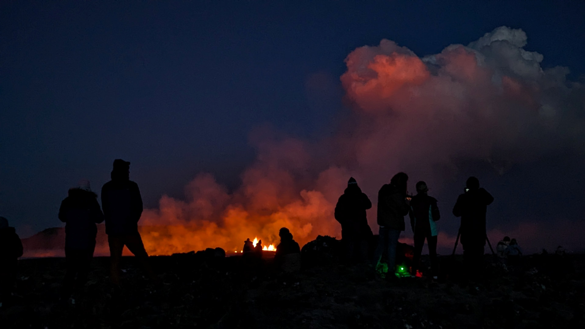 Menschen betrachten als schwarze Siluette Nachts einen Vulkanausbruch in Island