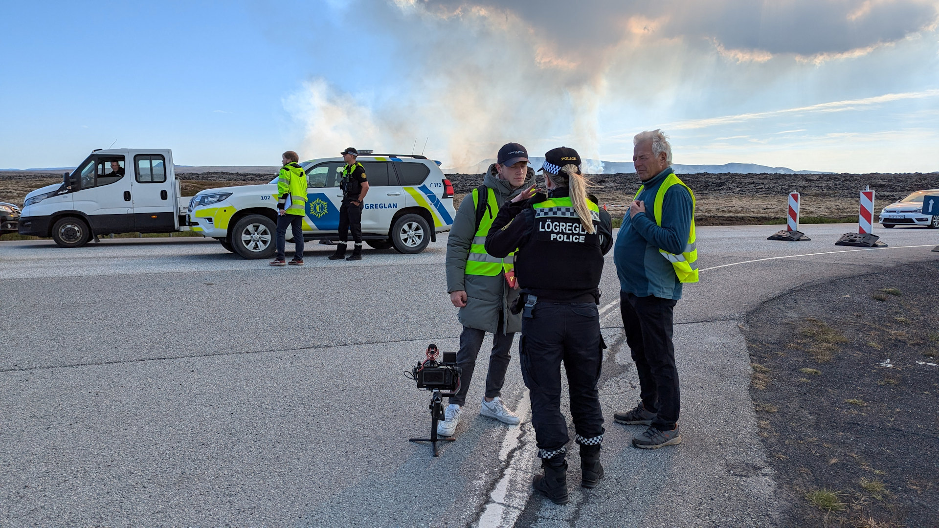 Zwei Journalisten mit gelber Warnweste  diskutieren in Island mit der Polizei