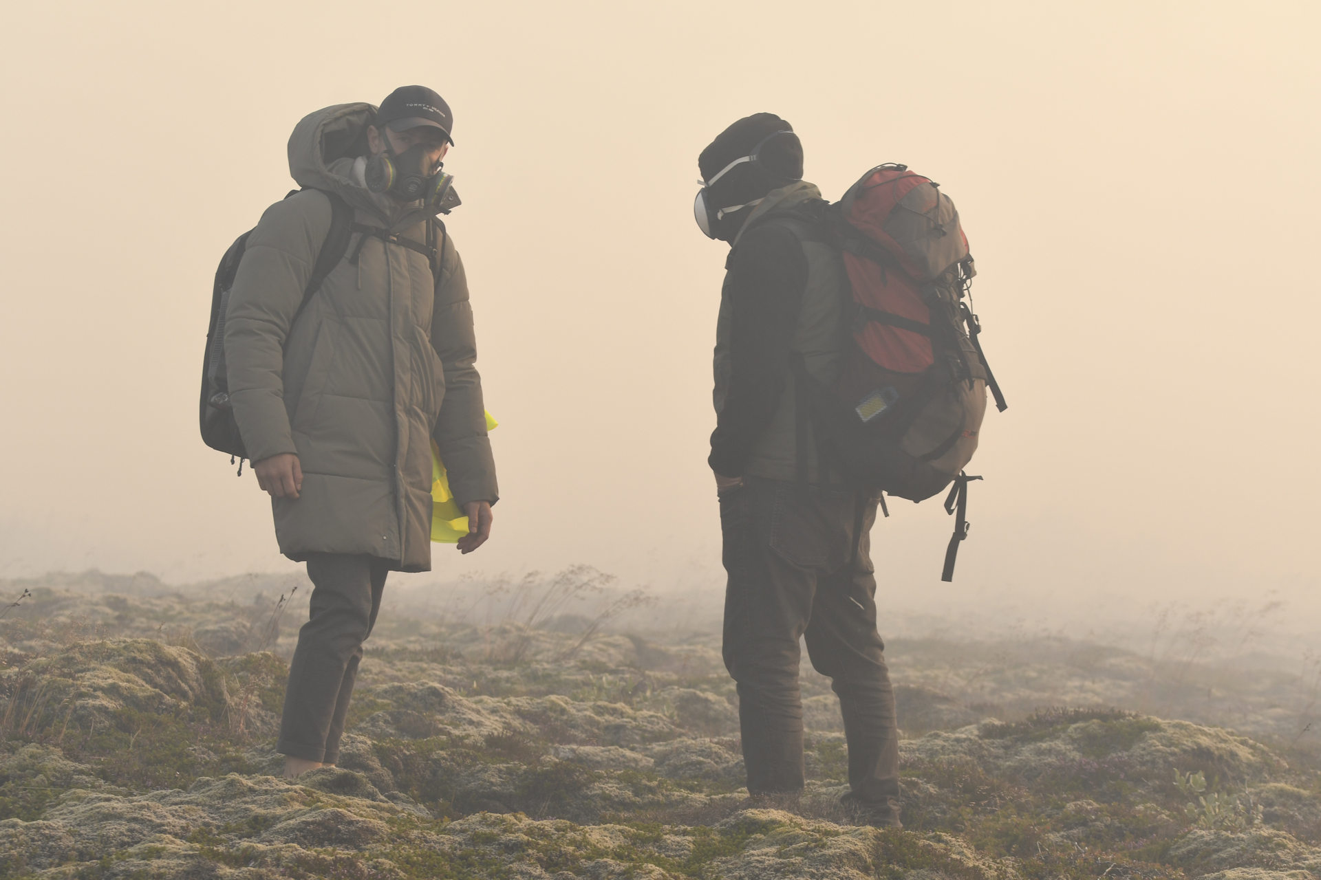 Zwei Wanderer in einem verqualmten Vulkangebiet mit Gasmaske