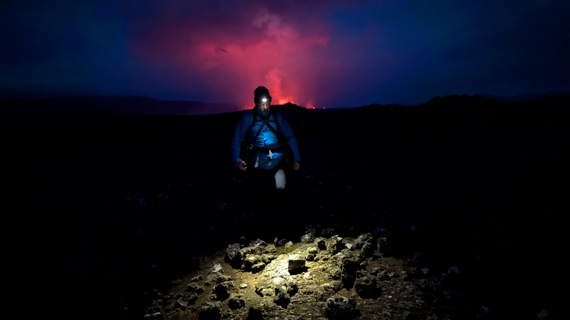 Ein Wanderer ist im Scheinwerferkegel einer Taschenlampe Nachts beim einem Vulkan in Island unterwegs