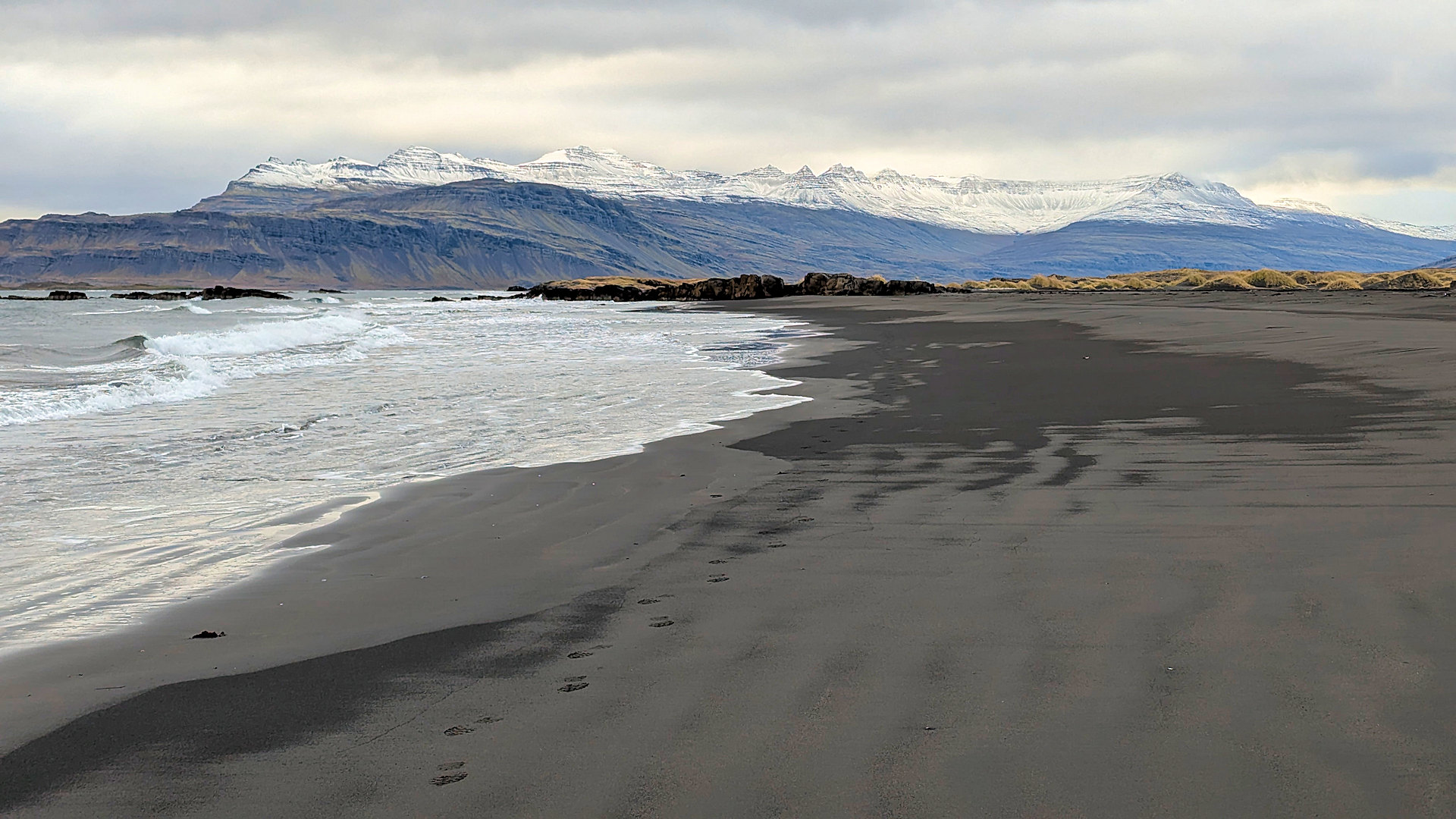 Schwarzer Sandstrand Djupivogur Island mit schneebedeckten Bergen im Hintergrund