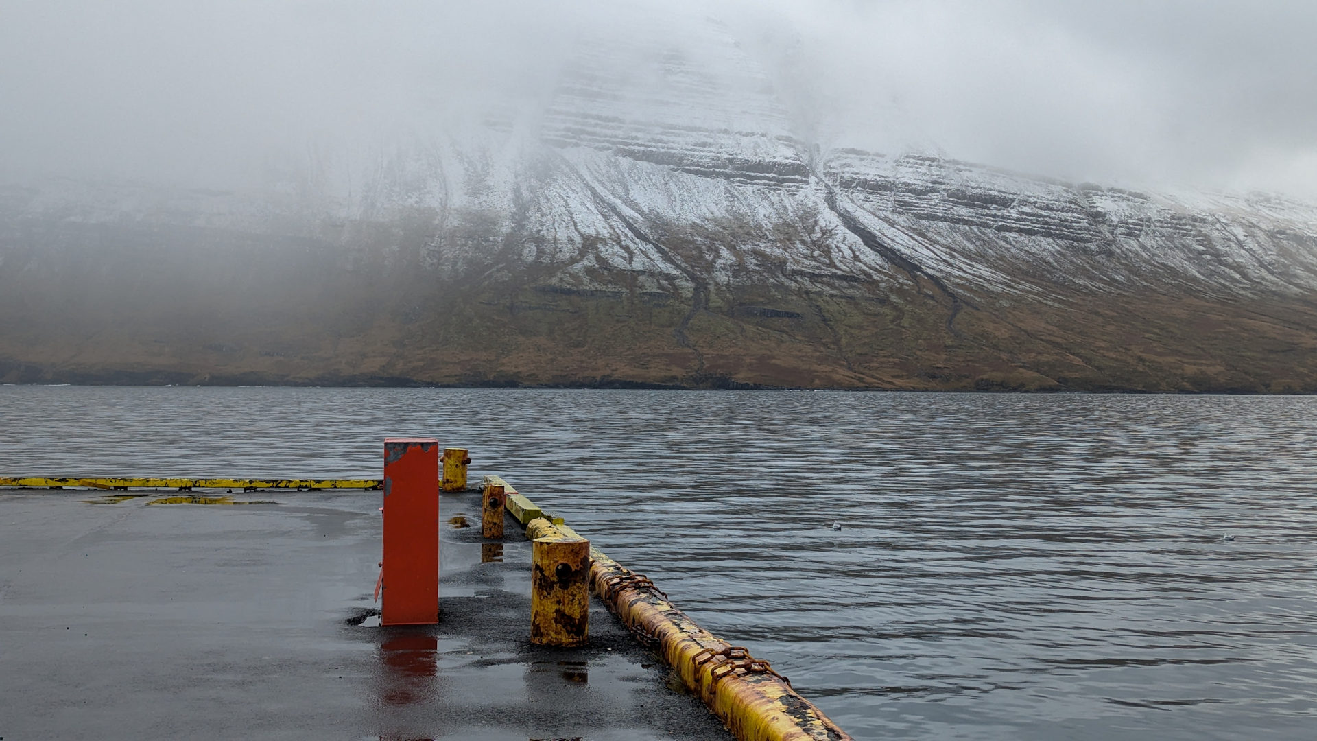 Anleger in einem Fjord in Island mit verschneiten Bergen im Hintergrund