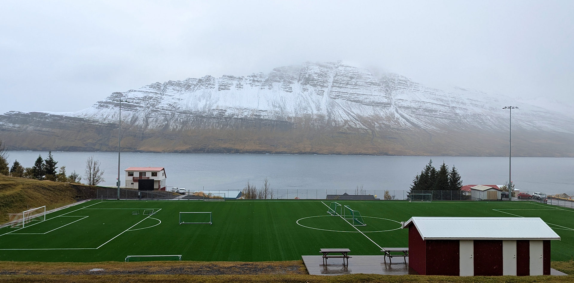 Grünes Fussballfeld in einem isländischen Fjord mit verschneiten Bergen