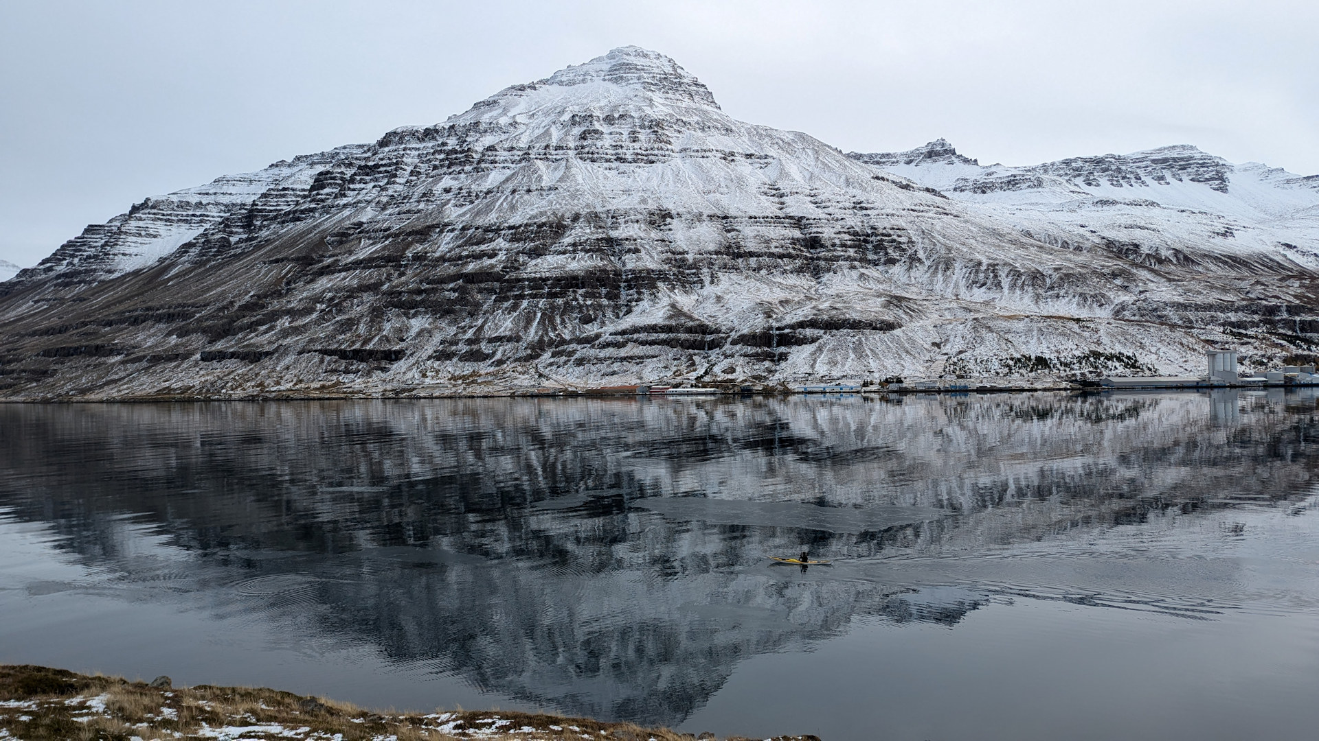 Ein Ruderer fährt im Wasser durch die Spiegelung eines verschneiten Berges in Seydisfjördur Island